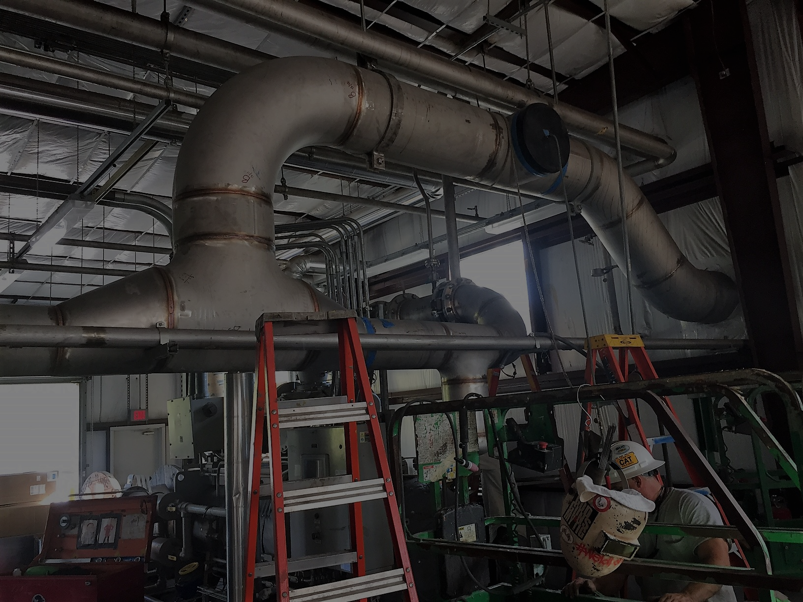 Field technician working near industrial piping for compressors, gas conditioning skids, and chiller systems in a gas processing facility.