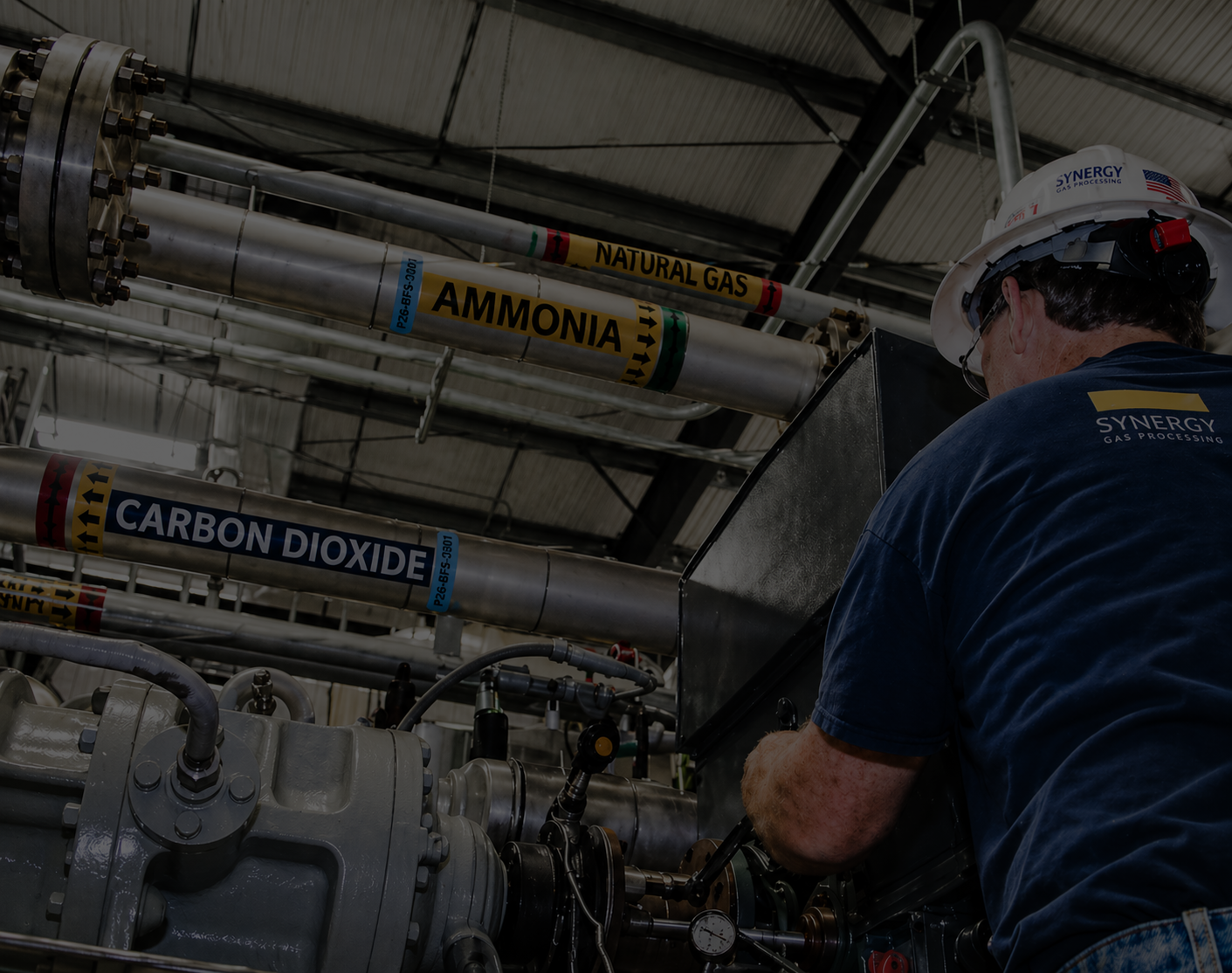 Synergy Gas Processing technician servicing industrial gas processing equipment with natural gas, ammonia, and carbon dioxide piping.